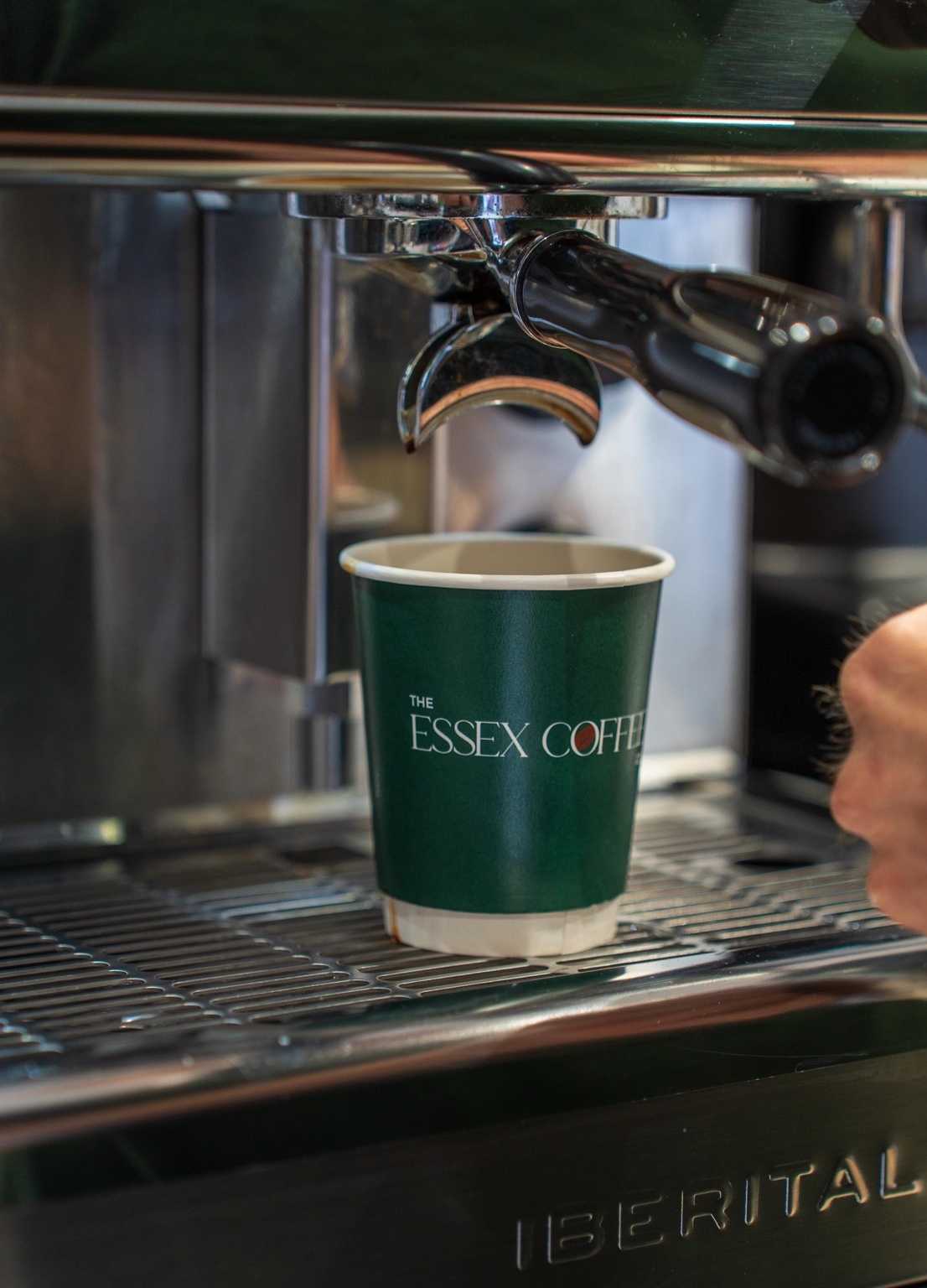 A dark green Essex Coffee Co. branded cup beneath the espresso machine group head.